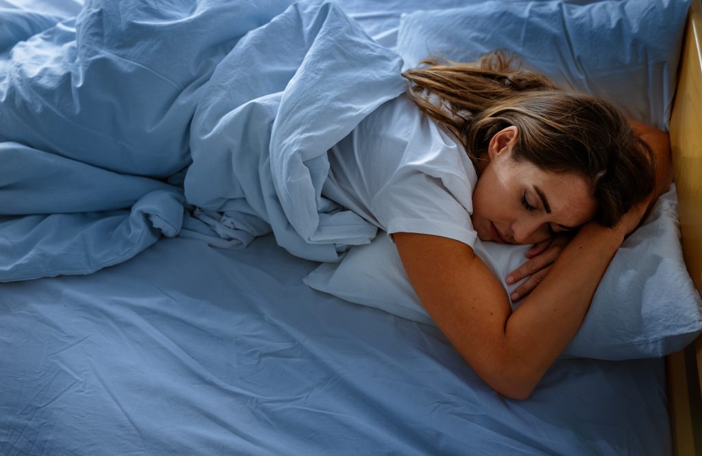A young woman sleeping peacefully in a comfortable bed with white linens, illustrating healthy sleep habits and wellness.